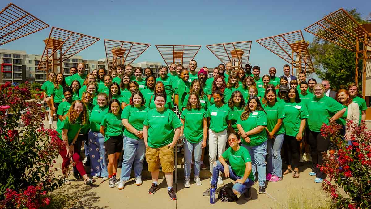 Large group of people outdoors wearing green shirts and posing for a photo
